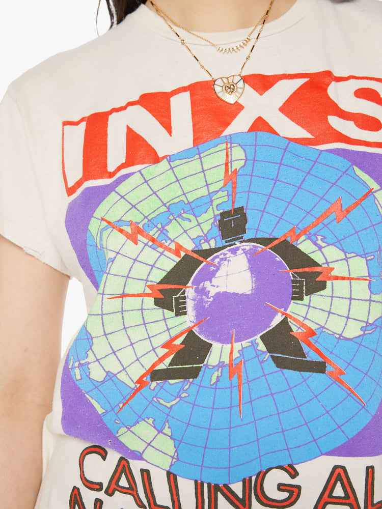 Close up view of a woman distressed crewneck tee in white, the tee pays homage to INXS' Calling All Nations tour with bold graphics on the front and back.
