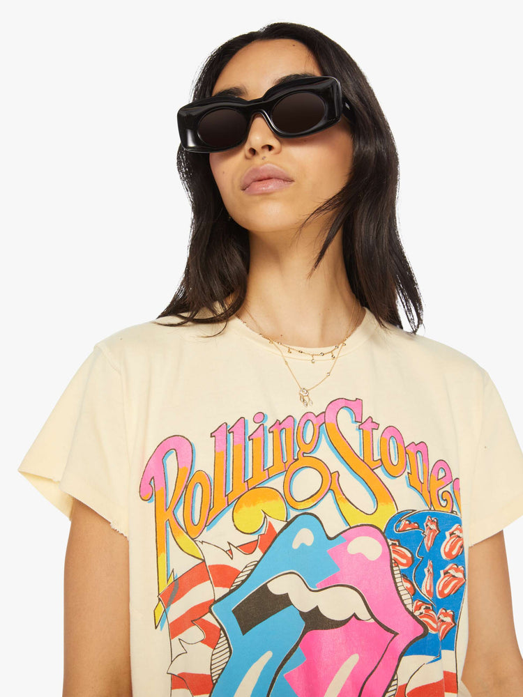 Close up view of a woman hand distressed crewneck tee in a pastel yellow hue the tee riffs on the Rolling Stones' Steel Wheels tour with the band's iconic tongue-and-lips logo on the front and tour dates on the back.