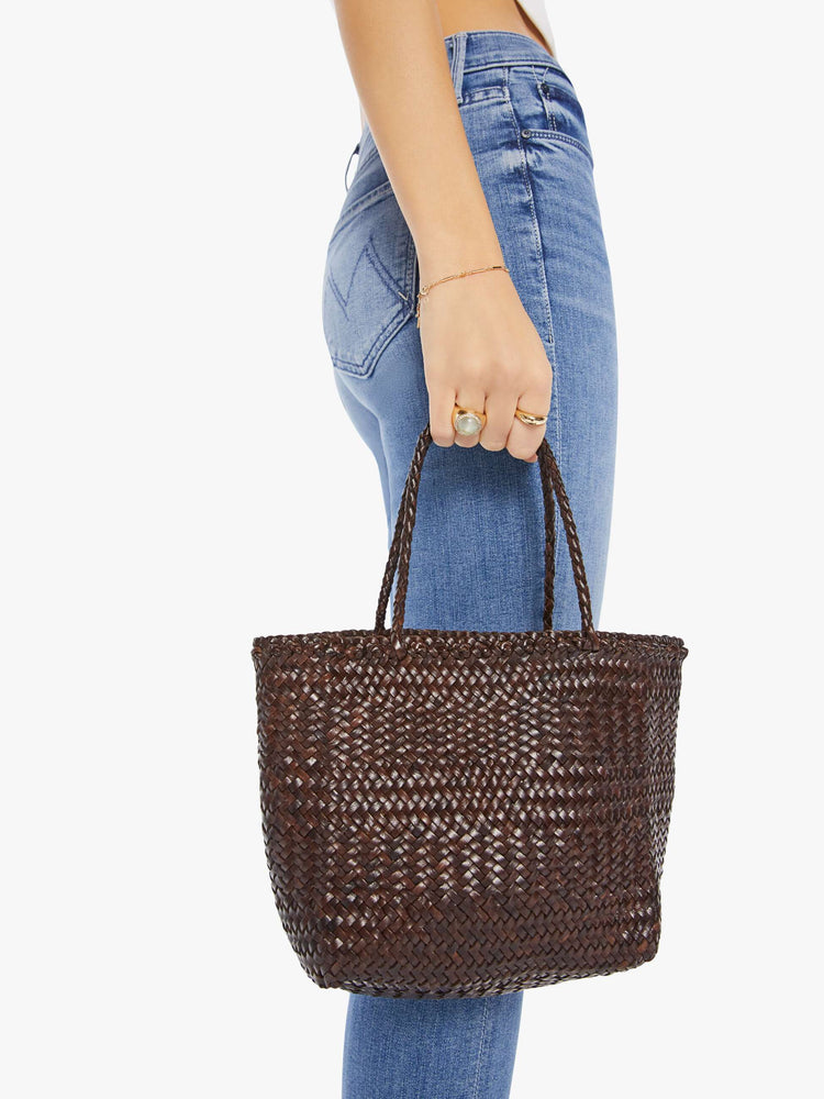 Side view of a woman holding a dark brown woven bag.