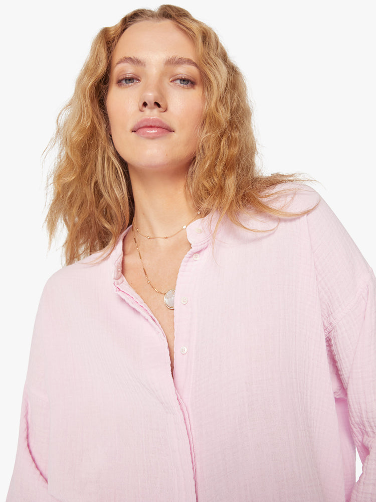 Close up view of a woman baby pink blouse with a V-neck with buttons down the front, a curved hem and an airy fit.