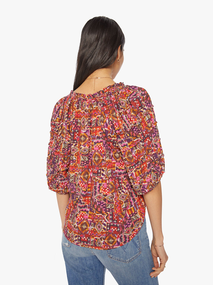 Back view of a woman colorful kaleidoscope print shirt in a deep Vneck, elbow-length balloon sleeves.