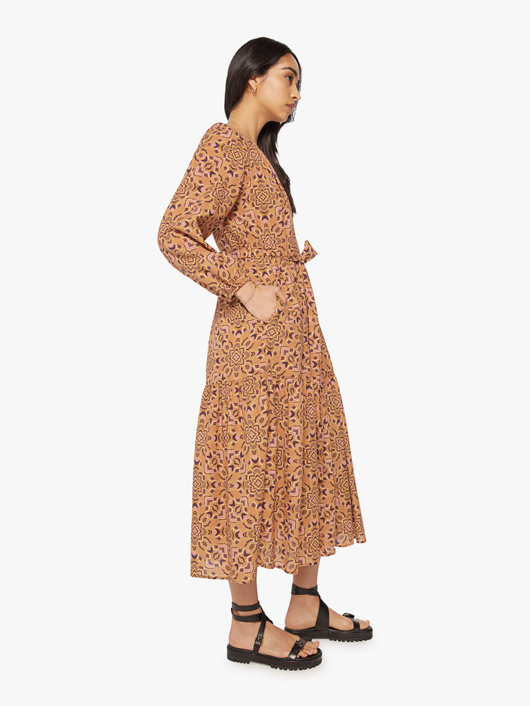 Side view of a woman midi vneck long sleeve dress made from 100% cotton in a golden-orange hue with a purple floral print with a tied waist.