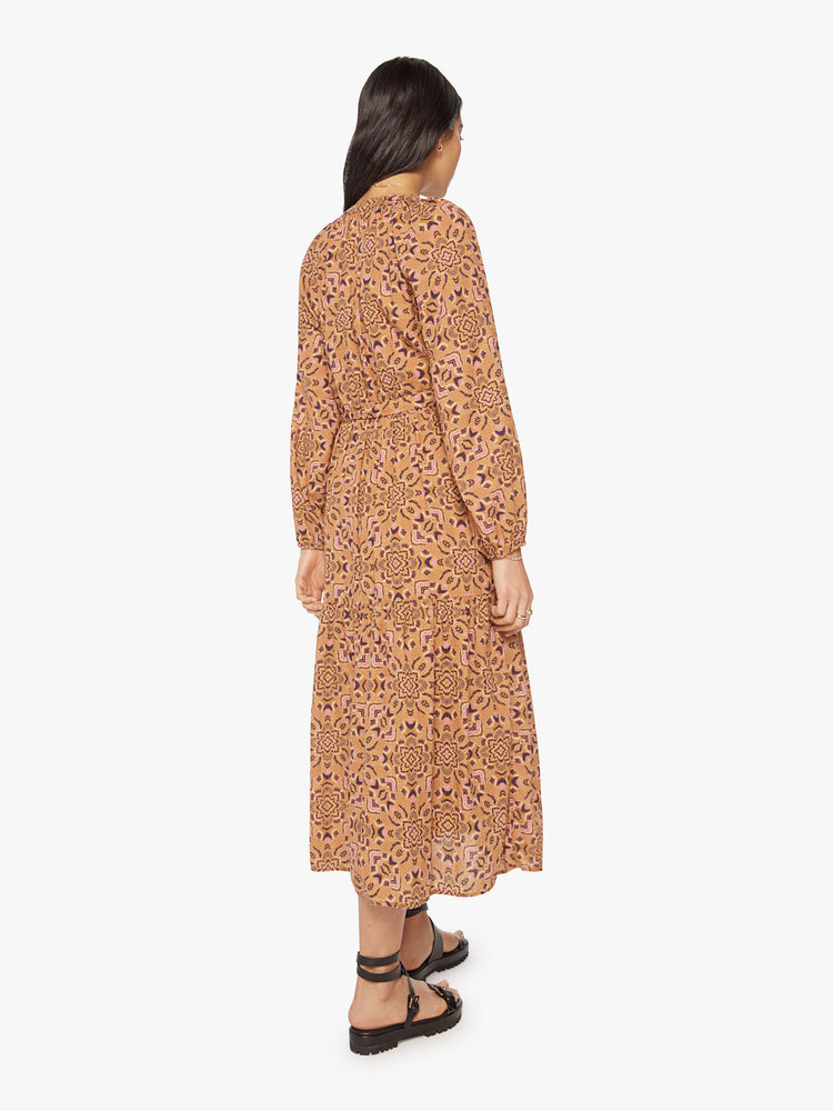Back view of a woman midi vneck long sleeve dress made from 100% cotton in a golden-orange hue with a purple floral print with a tied waist.