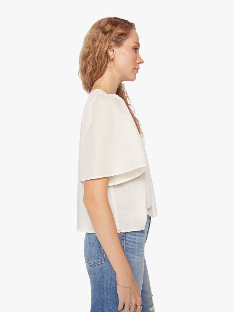 Side view of a woman pearly-white hue blouse with a vneck, short, boxy sleeves and a cropped hem.