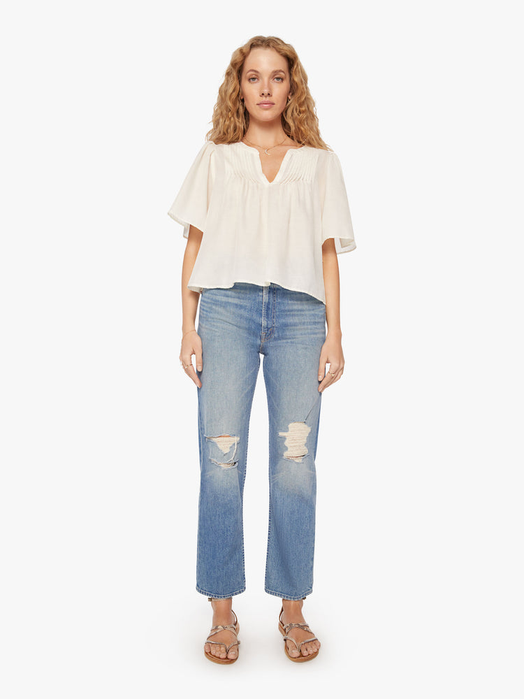 Full body view of a woman pearly-white hue blouse with a vneck, short, boxy sleeves and a cropped hem.
