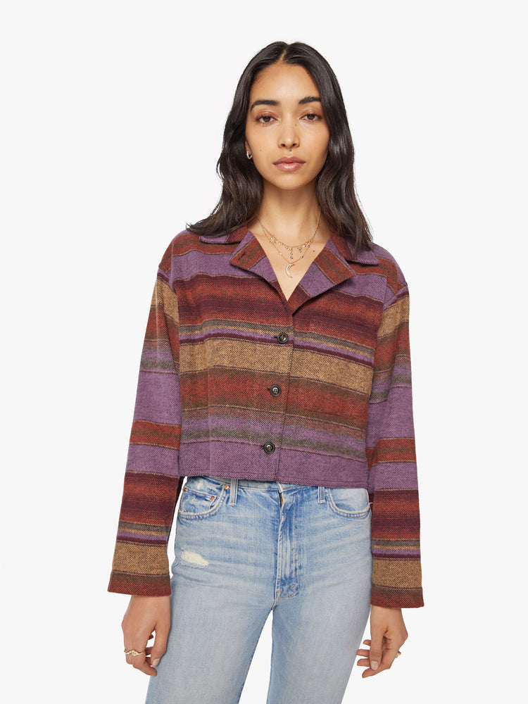 Front view of a woman in a deep burgundy, lavender and yellow horizontal stripe pattern jacket with a vneck, drop shoulders, button downs the front and a boxy fit.
