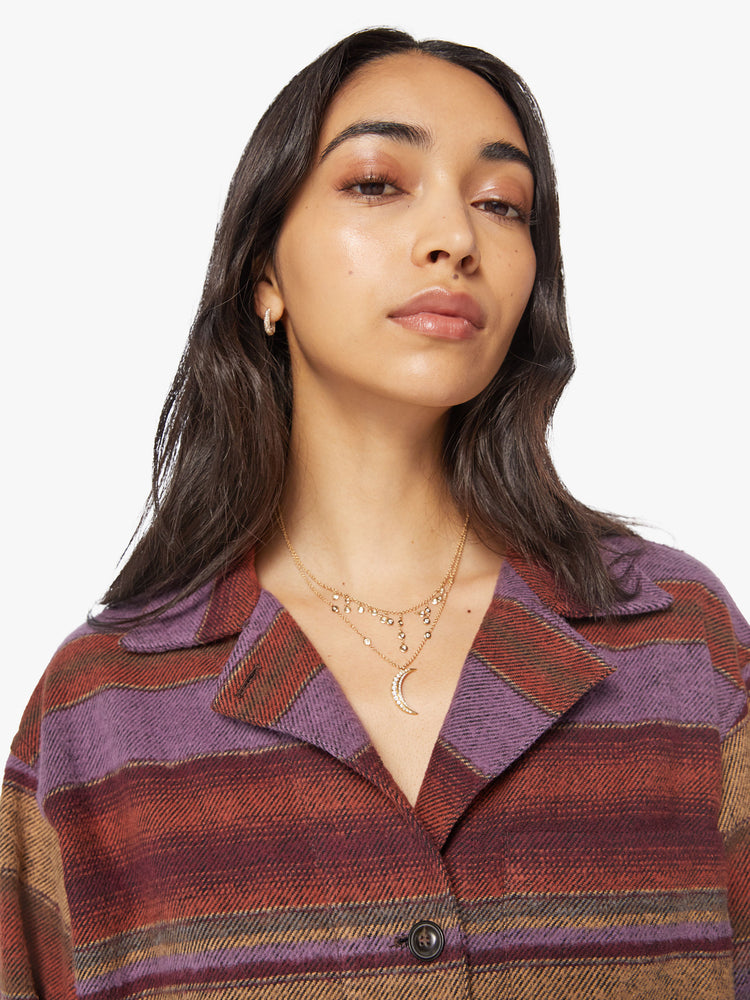 Close up view of a woman in a deep burgundy, lavender and yellow horizontal stripe pattern jacket with a vneck, drop shoulders, button downs the front and a boxy fit.