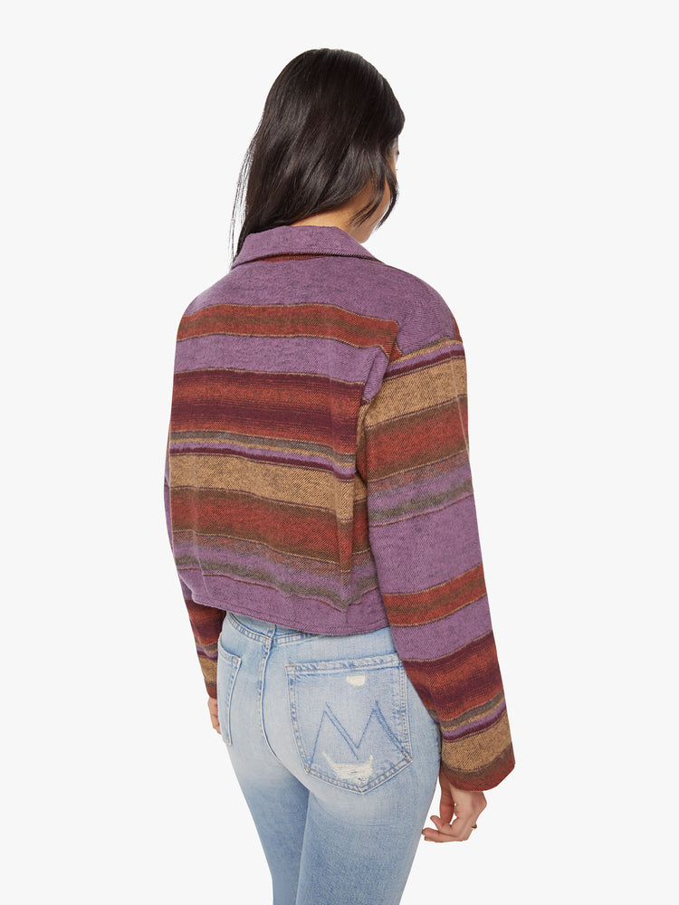Back view of a woman in a deep burgundy, lavender and yellow horizontal stripe pattern jacket with a vneck, drop shoulders, button downs the front and a boxy fit.