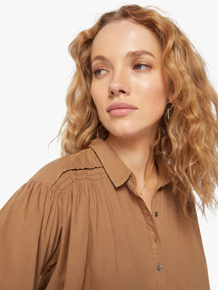 Close up view of a womans dark khaki sheer blouse with a buttoned V-neck, drop shoulders and a loose flowy fit.
