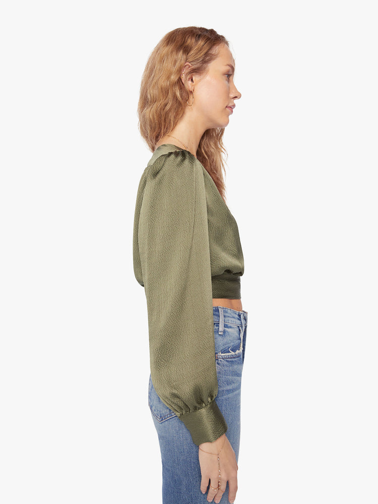 Side view of a womans shirt with a V-neck, long sleeves and a cropped hem that ties in an olive-green hue.