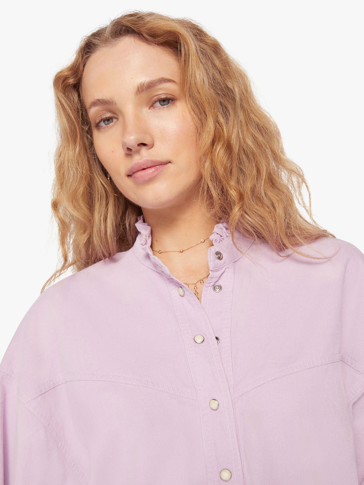 Close up view of a woman soft lilac shirt with a ruffled V-neck that buttons, drop shoulders, long sleeves, a cropped hem and a boxy fit.