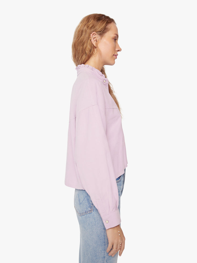 Side view of a woman soft lilac shirt with a ruffled V-neck that buttons, drop shoulders, long sleeves, a cropped hem and a boxy fit.