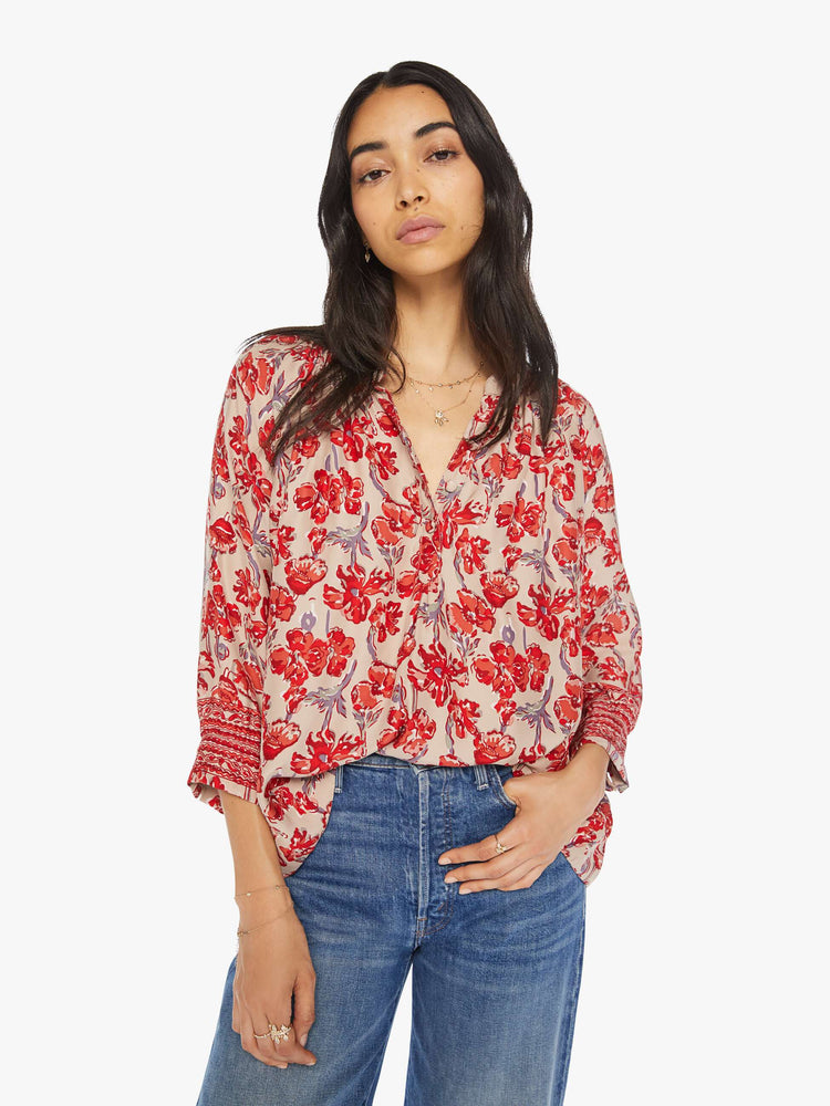 Front view of a woman nude with red floral top with a V-shaped neckline with covered buttons and subtle pleats below the collar.