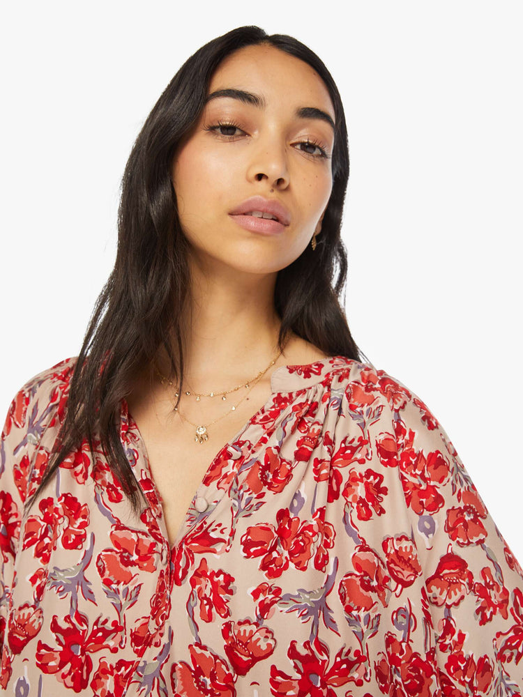Close up view of a woman nude with red floral top with a V-shaped neckline with covered buttons and subtle pleats below the collar.