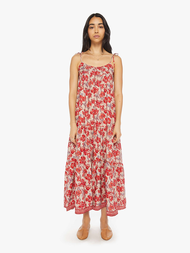 Front view of a woman dress features slim adjustable ties at the shoulders and a floaty, tiered skirt that emphasizes the relaxed fit in a nude and red floral print.