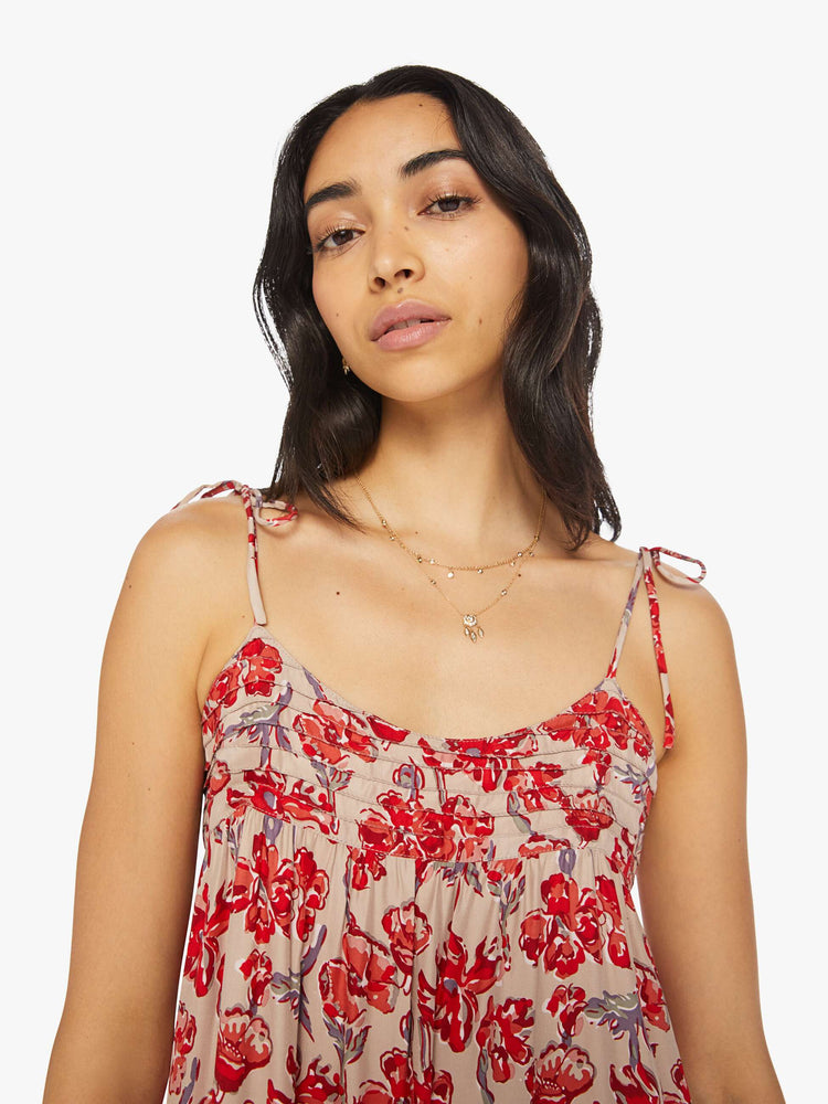 Close up view of a woman dress features slim adjustable ties at the shoulders and a floaty, tiered skirt that emphasizes the relaxed fit in a nude and red floral print.