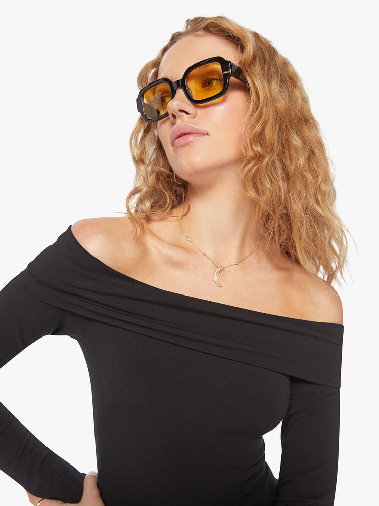 Close up view of a black off-the-shoulder midi dress with long sleeves and a calf-length hem with slim flit.