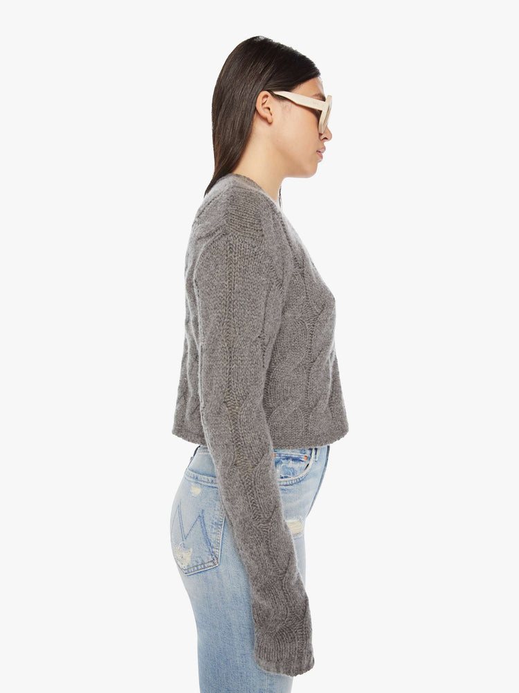 Side view of a woman dark grey hue with cable knit details cropped sweater designed with a V-neck, buttons down the front and a slim, cropped fit.