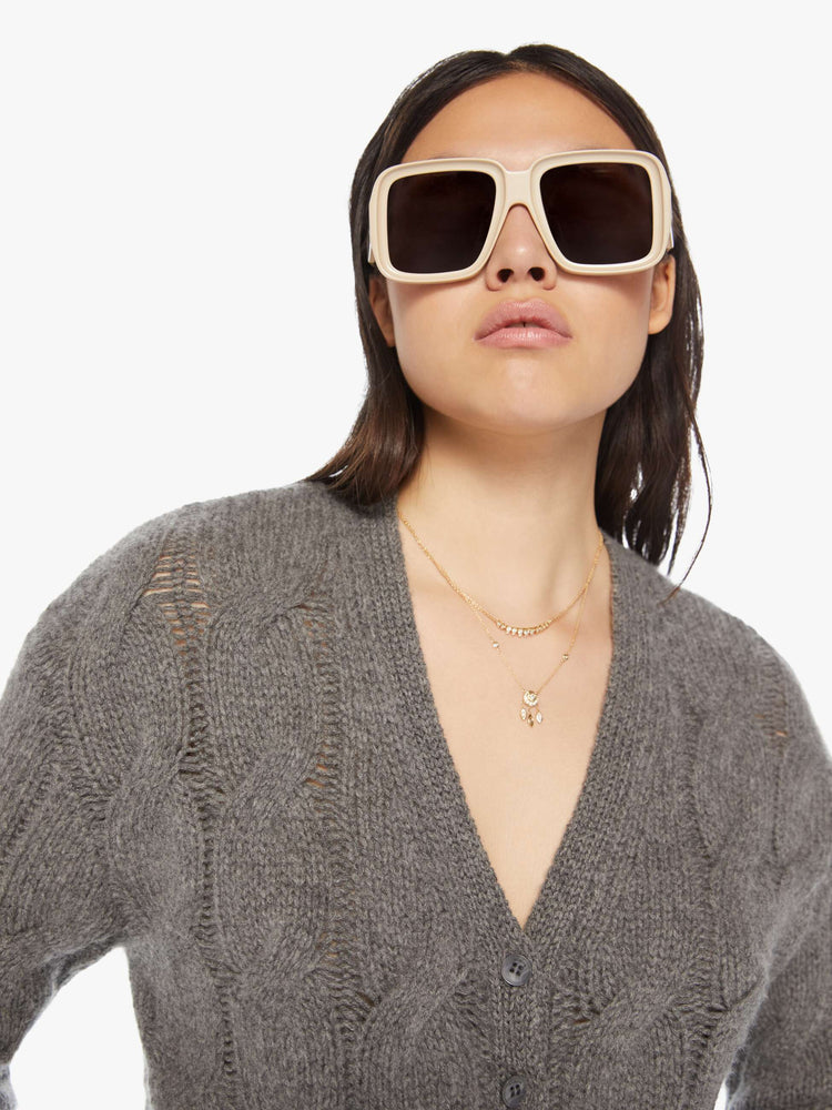 Close up view of a woman dark grey hue with cable knit details cropped sweater designed with a V-neck, buttons down the front and a slim, cropped fit.