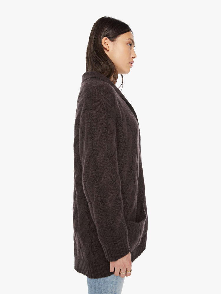 Side view of a woman brown oak hue oversized cardigan designed with a shawl collar, front patch pockets, buttons down the front, and a boxy, oversized fit.