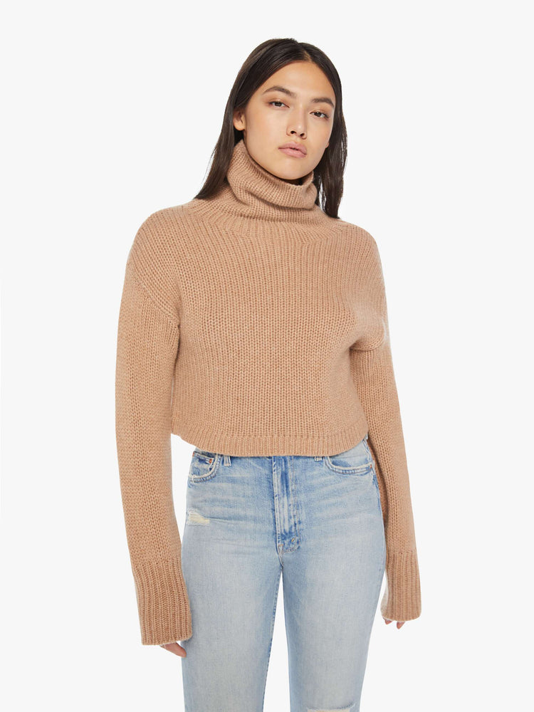 Front view of an almond hue cropped turtleneck sweater is designed with a folded neck, drop shoulders, ribbed hems and a boxy fit.