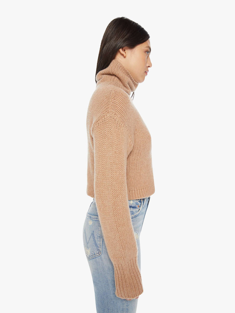 Side view of an almond hue cropped turtleneck sweater is designed with a folded neck, drop shoulders, ribbed hems and a boxy fit.