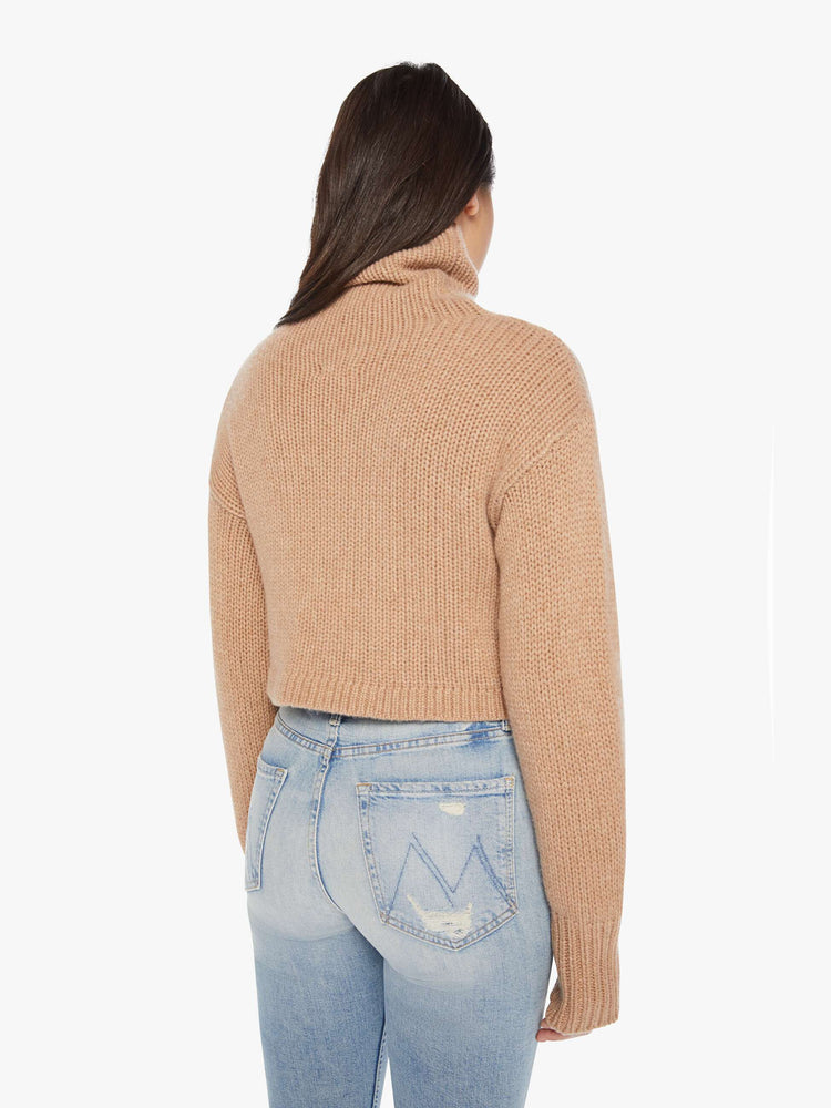Back view of an almond hue cropped turtleneck sweater is designed with a folded neck, drop shoulders, ribbed hems and a boxy fit.