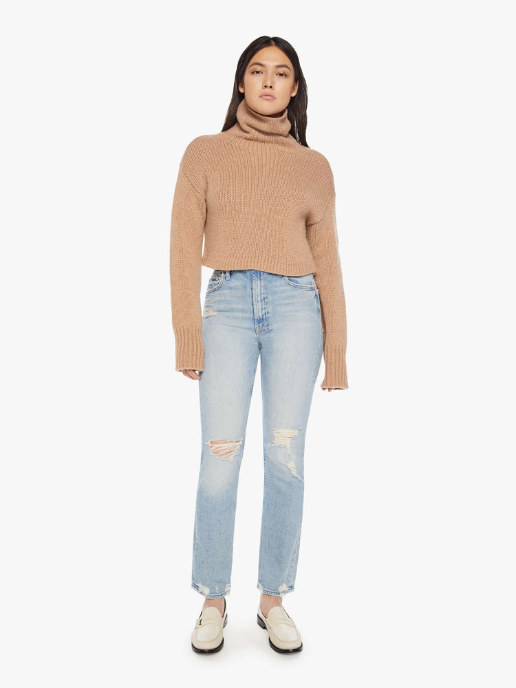 Full body view of an almond hue cropped turtleneck sweater is designed with a folded neck, drop shoulders, ribbed hems and a boxy fit.