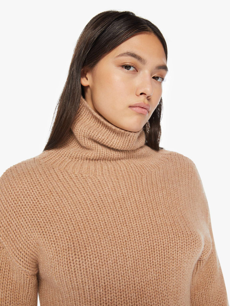 Close up view of an almond hue cropped turtleneck sweater is designed with a folded neck, drop shoulders, ribbed hems and a boxy fit.