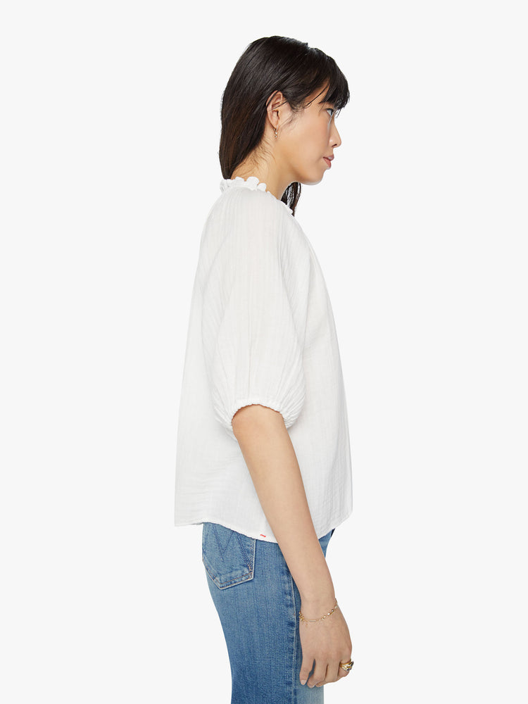 Side view of a woman white shirt with deep V-neck, elbow-length balloon sleeves and a loose fit.