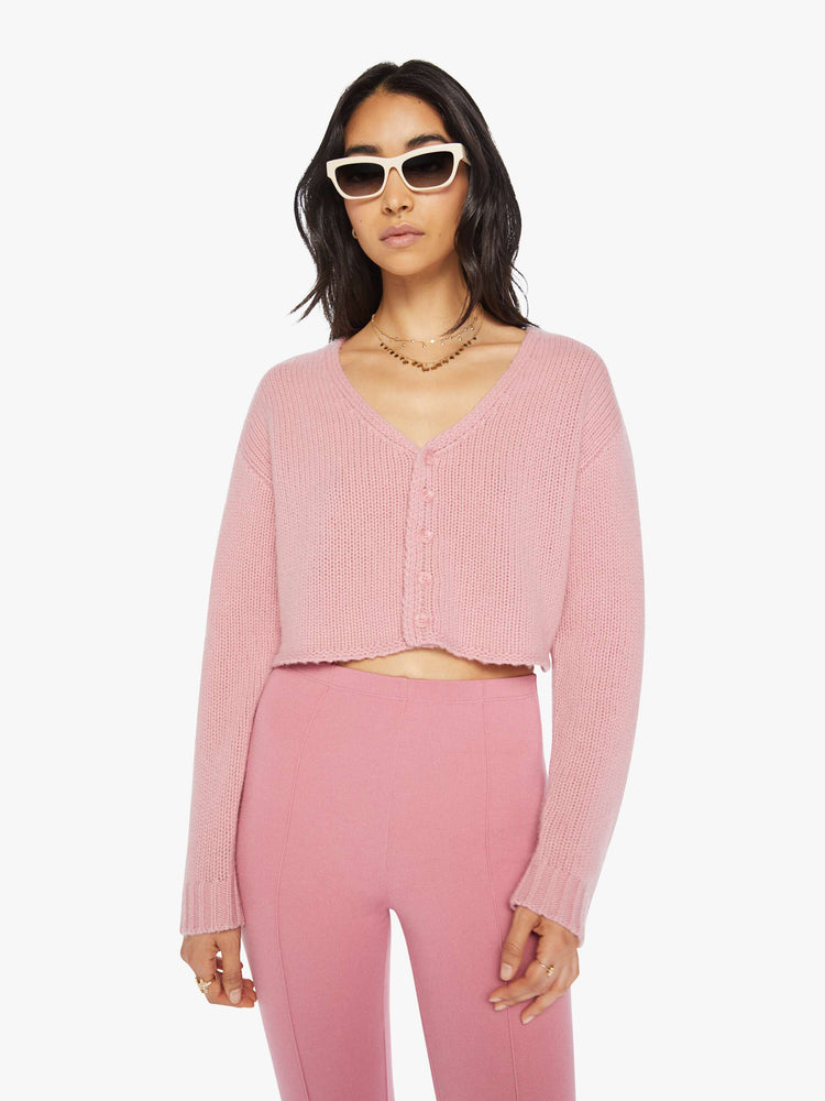 Front view of a woman pink cropped sweater with a V-neck, buttons down the front, drop shoulders and a cropped fit.