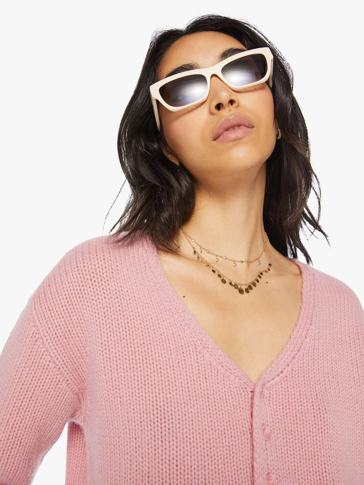 Close up view of a woman pink cropped sweater with a V-neck, buttons down the front, drop shoulders and a cropped fit.