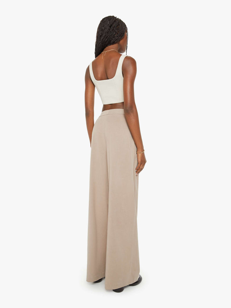 Back view of woman brown hue pants are designed with a buttoned waistband, front pleats, side slit pockets and a wide leg.