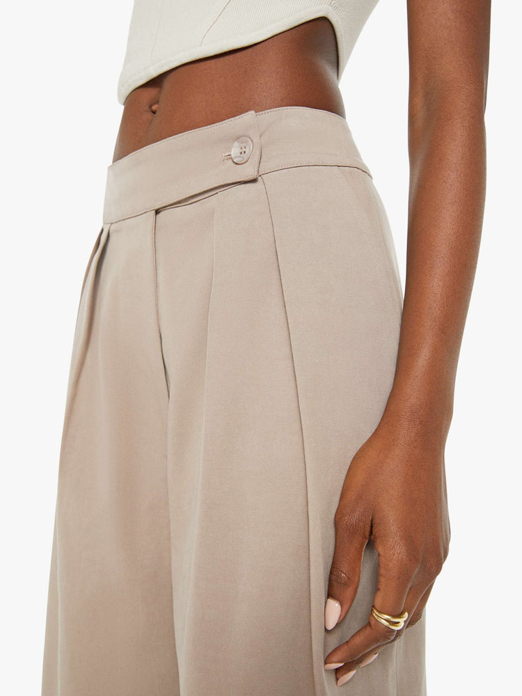 Waist close up view of woman brown hue pants are designed with a buttoned waistband, front pleats, side slit pockets and a wide leg.