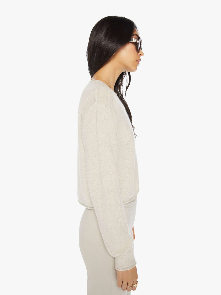 Side view of a woman off white sweater with a crewneck, drop shoulders, stacked long sleeves and a cropped hem.