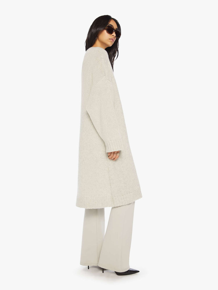 Side view of woman in off white oversized cardigan with an open front, shawl collar and a knee-length hem.