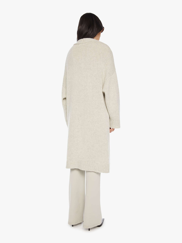 Back view of woman in off white oversized cardigan with an open front, shawl collar and a knee-length hem.