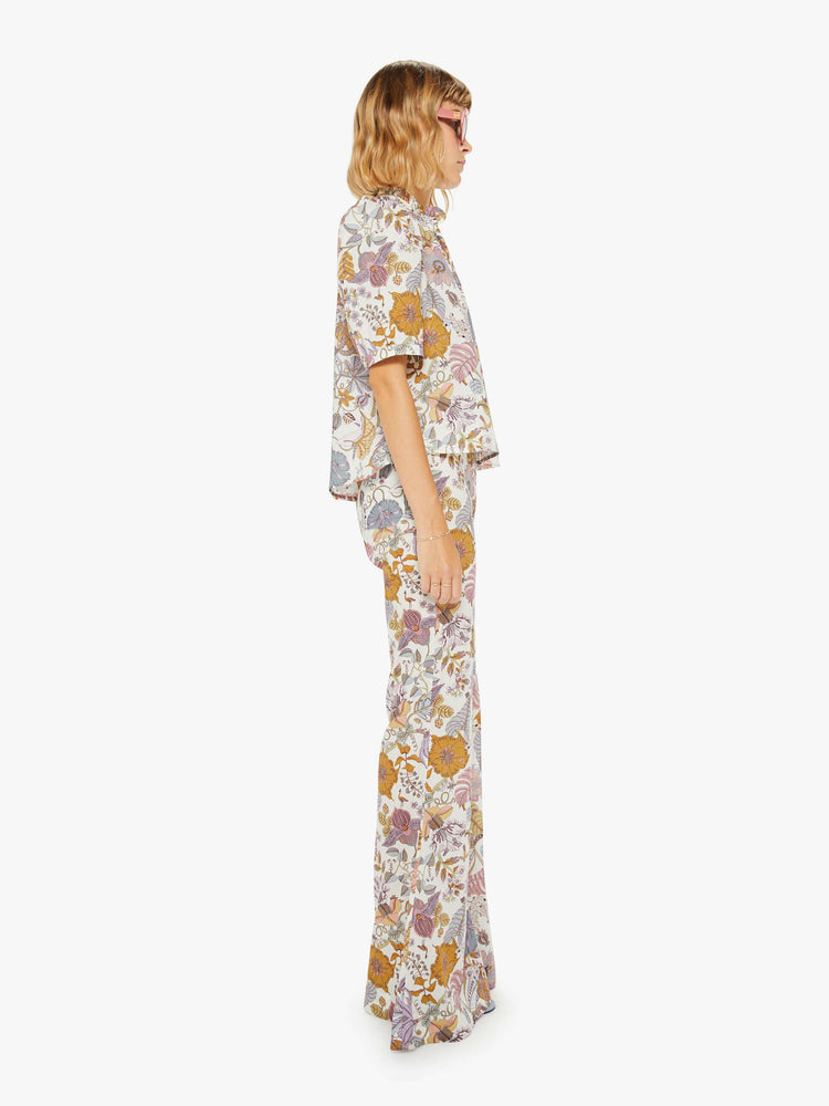 Side view of a woman colorful floral print, and feature a high rise, flared leg and a long inseam.
