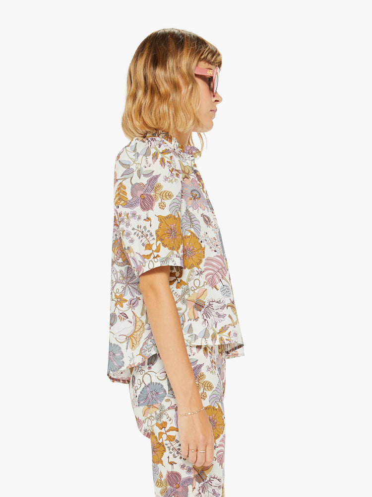 Side view of a woman shirt in a colorful floral print with a buttoned V-neck, stacked collar, short balloon sleeves and ruffles.