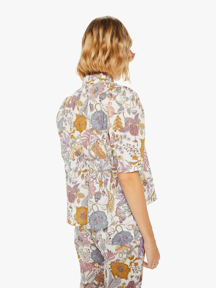 Back view of a woman shirt in a colorful floral print with a buttoned V-neck, stacked collar, short balloon sleeves and ruffles.