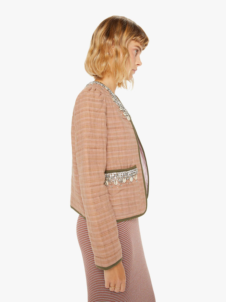 Side view of a woman jacket in a pink stripe pattern with dark green trim and shell and gem applique at the collar and pockets with a V-neck, tie closure, puffed sleeves and a boxy fit.