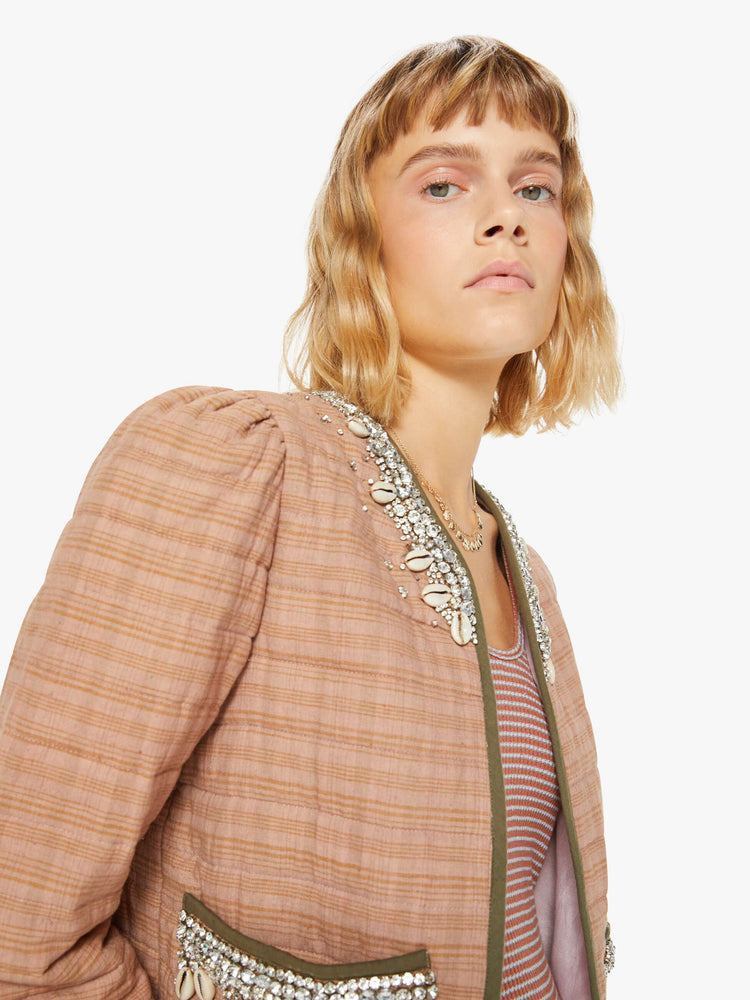 Close up view of a woman jacket in a pink stripe pattern with dark green trim and shell and gem applique at the collar and pockets with a V-neck, tie closure, puffed sleeves and a boxy fit.