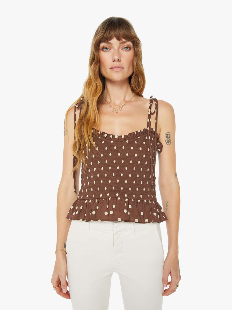 Front view of a woman brown and white polka dots blouse with  tied spaghetti straps, a V-neck, smocked bodice and ruffled trim.