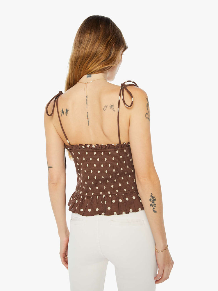 Back view of a woman brown and white polka dots blouse with tied spaghetti straps, a V-neck, smocked bodice and ruffled trim.
