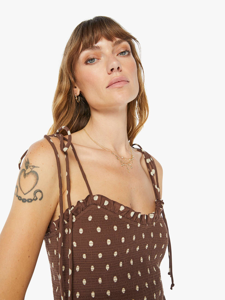 Close up view of a woman brown and white polka dots blouse with tied spaghetti straps, a V-neck, smocked bodice and ruffled trim.