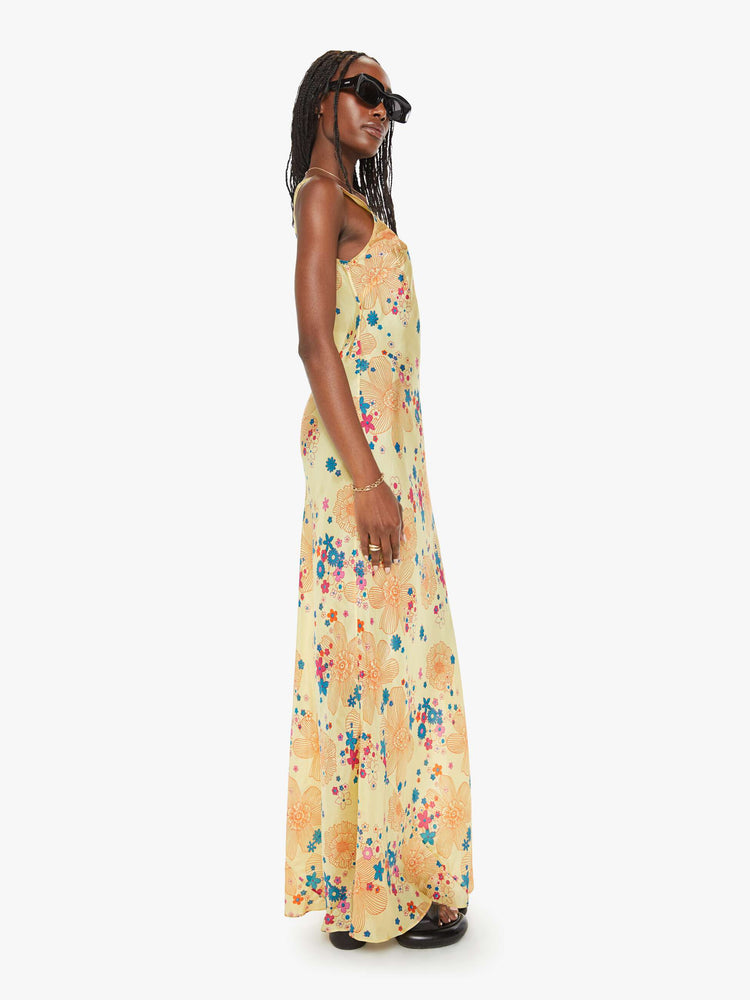 Side view of a woman pastel yellow with a colorful floral print, and features a scoop neck, narrow fit and an ankle-length hem.
