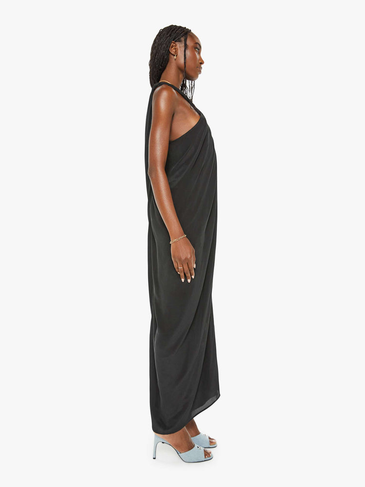 Side view of a woman black dress with a wrapped halter neck, gathered seam down the front and a long ankle-length hem.