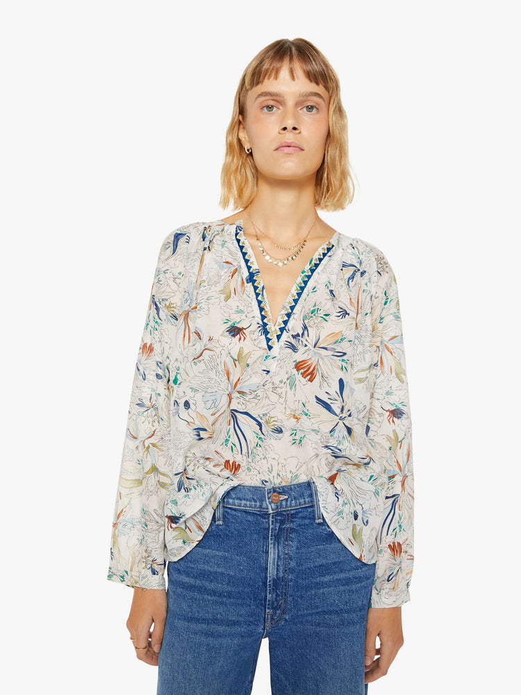 Front view of a woman blouse with a deep V-neck, long sleeves and flowy fit in off white with colorful floral print and blue trim.