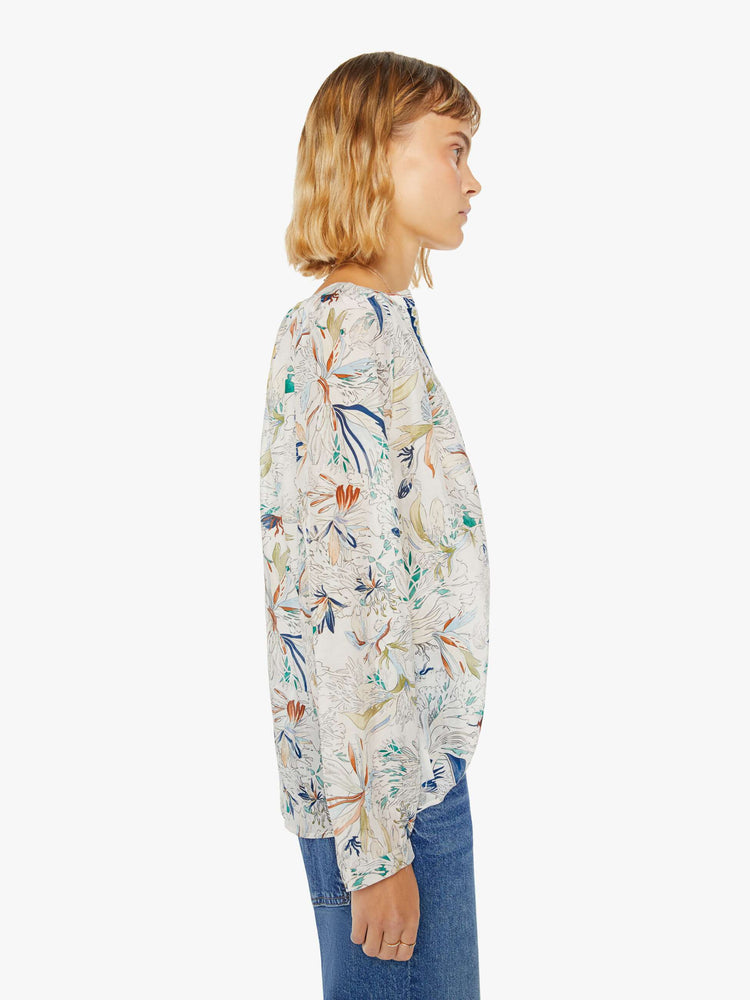 Side view of a woman blouse with a deep V-neck, long sleeves and flowy fit in off white with colorful floral print and blue trim.