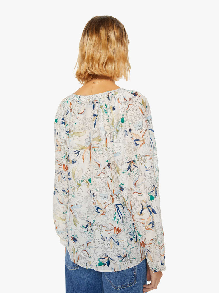 Back view of a woman blouse with a deep V-neck, long sleeves and flowy fit in off white with colorful floral print and blue trim.
